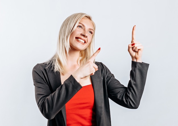 Retrato de una mujer sonriente apuntando con el dedo hacia arriba y sonríe sobre fondo gris aislado