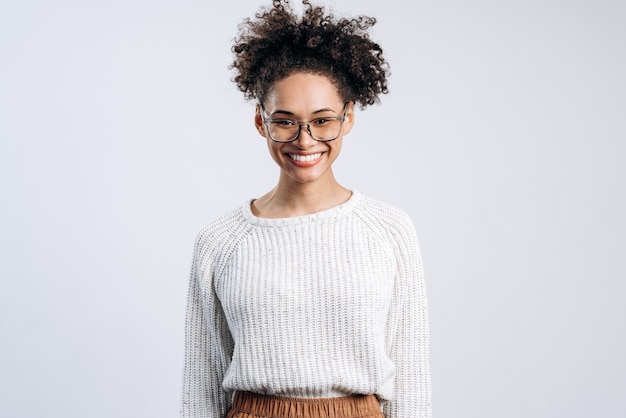 Retrato de mujer sonriente con cabello ondulado que expresa emociones positivas y felicidad, mientras mira a la cámara y está de buen humor. Tiro de estudio interior aislado sobre fondo blanco.