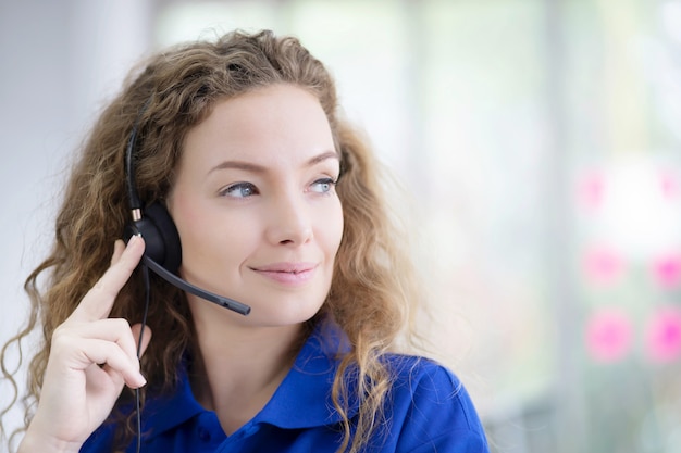 Retrato de mujer sonriente con camisa azul trabajando con auriculares.