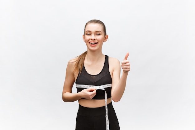 Retrato de mujer sonriente caucásica atractiva con cinta métrica y mostrando el pulgar hacia arriba