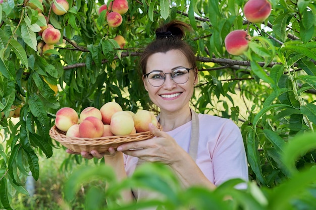 Retrato de mujer sonriente con cesta de duraznos frescos con fondo de duraznos maduros