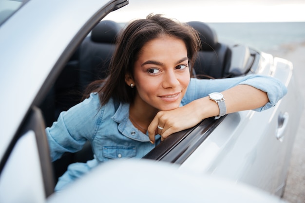 Foto retrato de mujer sonriente conduciendo un coche convertible en la playa