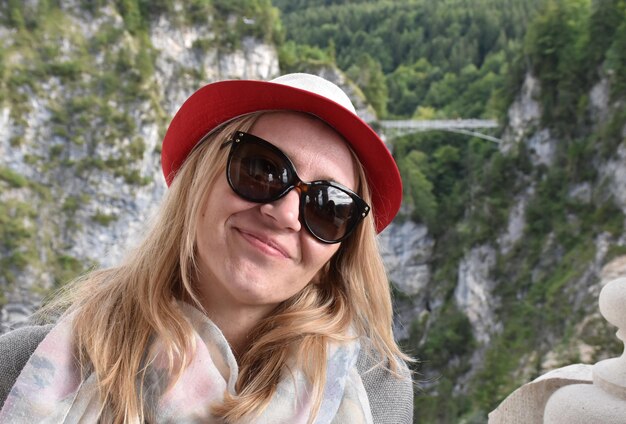 Foto retrato de una mujer sonriente con gafas de sol contra las montañas