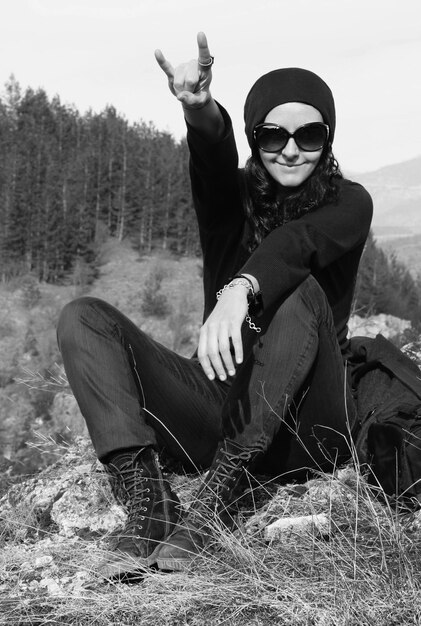 Foto retrato de una mujer sonriente gestando el signo del cuerno en el campo