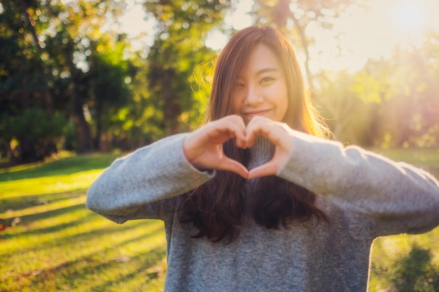 Retrato de una mujer sonriente haciendo forma de corazón mientras está de pie en el parque