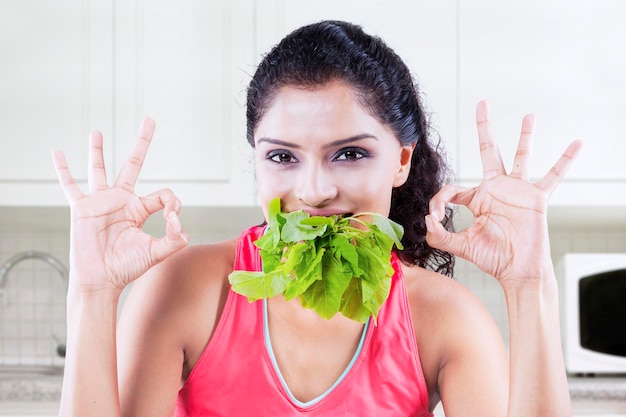 Retrato de una mujer sonriente haciendo gestos mientras come verduras de hoja en casa