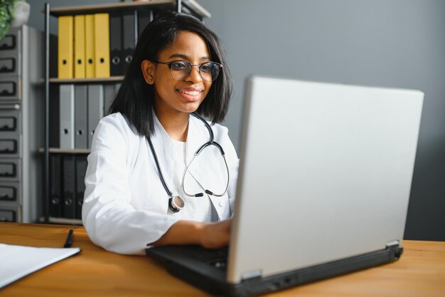 Retrato de mujer sonriente médico vistiendo bata blanca con estetoscopio en la oficina del hospital