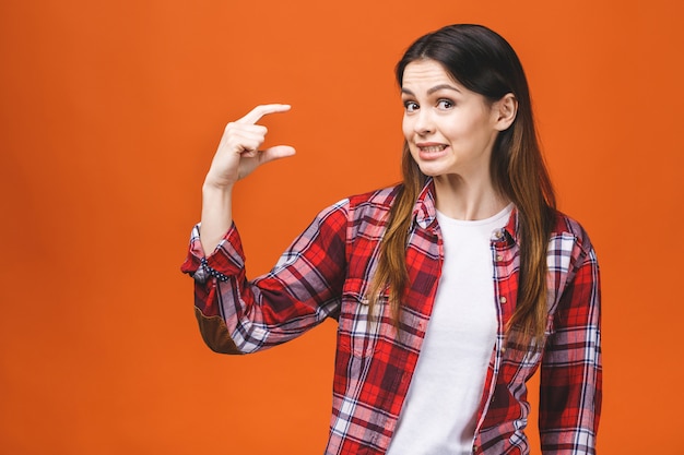 Retrato de mujer sonriente mostrando pequeña cantidad de algo, aislado sobre fondo naranja.