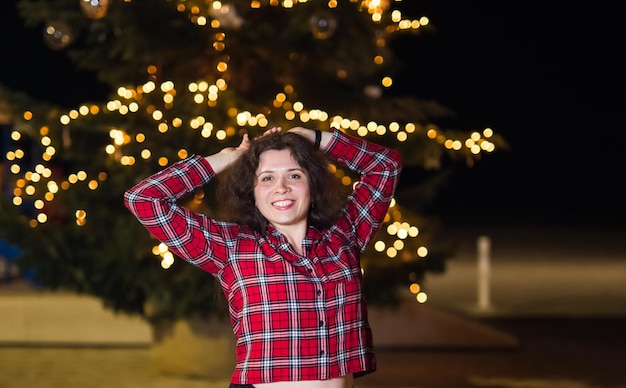 Foto retrato de una mujer sonriente de pie contra las luces de navidad iluminadas