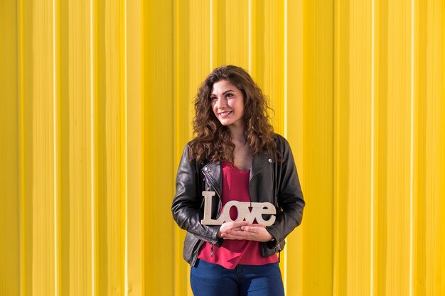 Foto retrato de una mujer sonriente de pie contra una pared amarilla