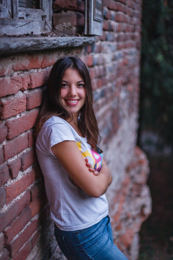 Foto retrato de una mujer sonriente de pie contra una pared de ladrillo