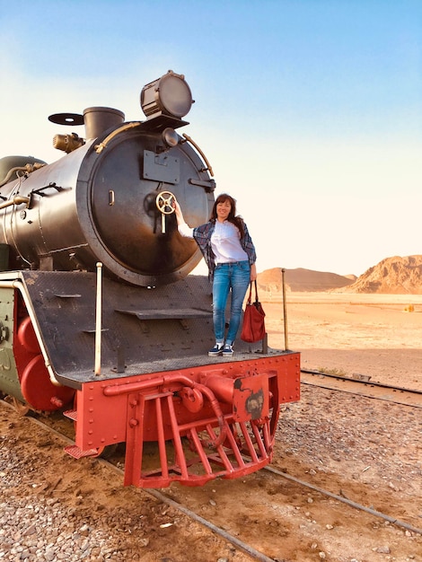 Foto retrato de una mujer sonriente de pie en un tren de vapor en el desierto