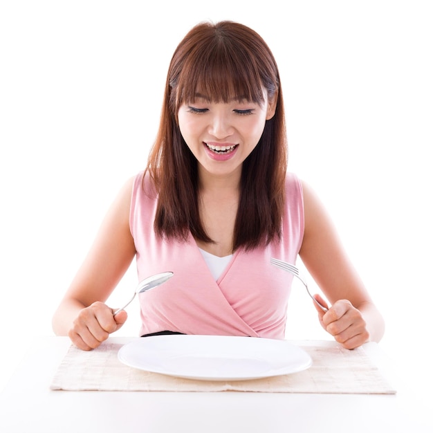 Retrato de una mujer sonriente con un plato vacío y cubiertos contra un fondo blanco