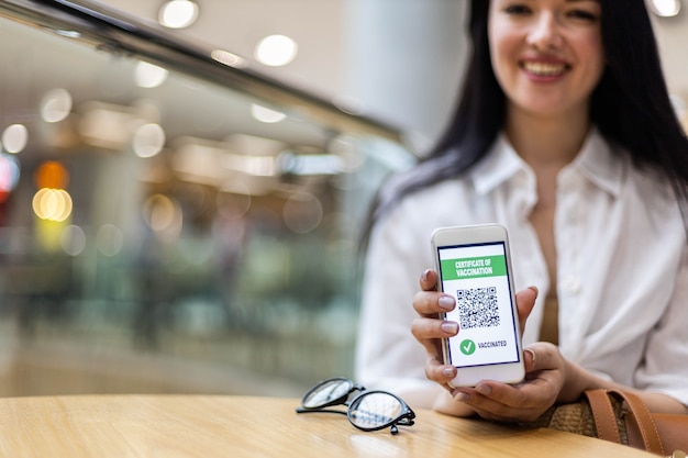 Retrato de mujer sonriente posando con certificado de vacuna en la pantalla del teléfono inteligente prevención del coronavirus