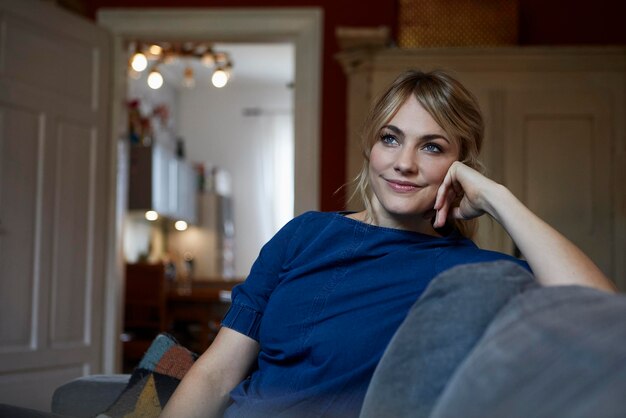 Retrato de mujer sonriente relajándose en el sofá en casa