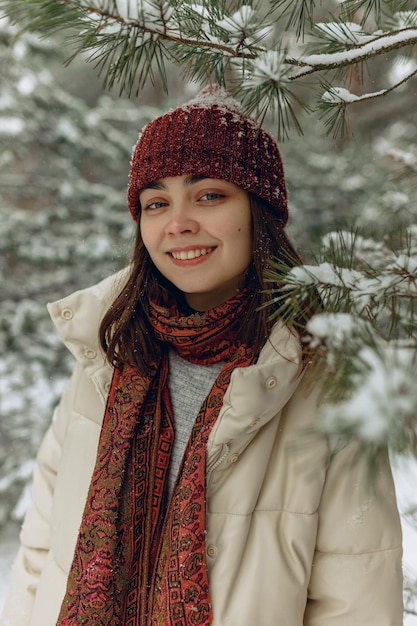 Retrato de mujer sonriente en ropa de abrigo de pie cerca de un árbol nevado en el parque de invierno