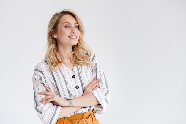 Retrato de mujer sonriente rubia vistiendo ropa casual mirando a un lado copyspace con los brazos cruzados aislado sobre la pared blanca