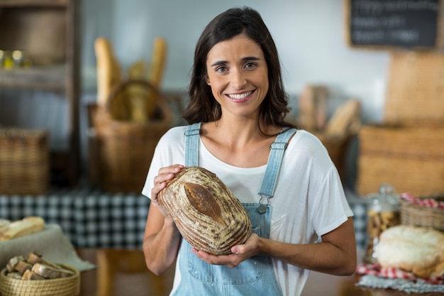 Foto retrato de mujer sonriente sentada en el mostrador sosteniendo una hogaza de pan redondo