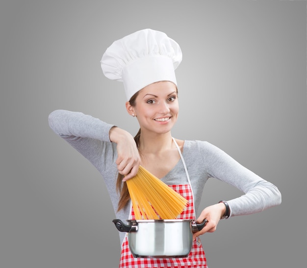 Retrato de una mujer sonriente con sombrero de chef agregando la pasta a la olla