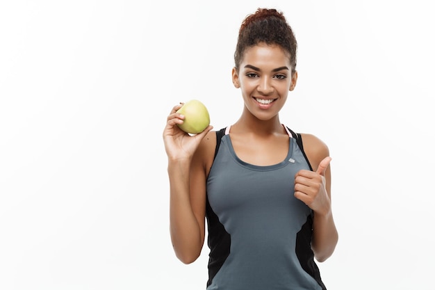 Foto retrato de una mujer sonriente sosteniendo una manzana mientras hace pulgares hacia arriba contra un fondo blanco