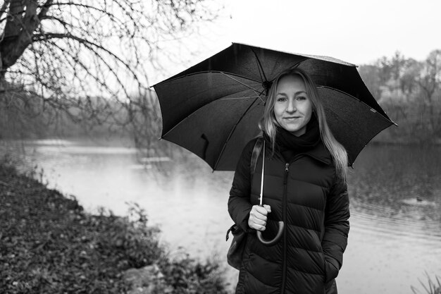 Foto retrato de una mujer sonriente sosteniendo un paraguas mientras está de pie contra el lago