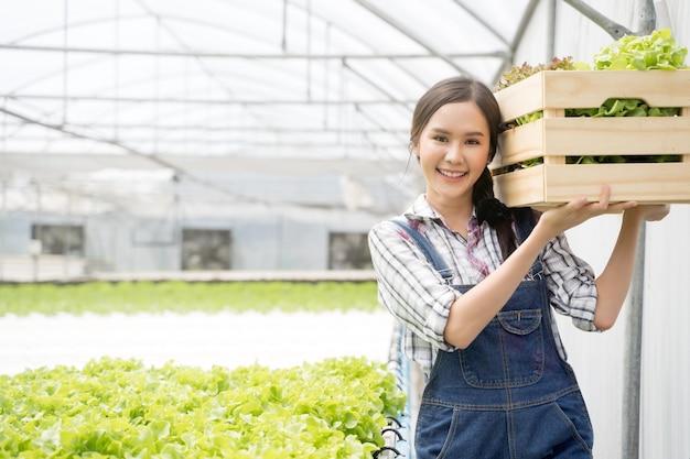 Retrato de una mujer sonriente sosteniendo un recipiente con verduras en una granja.