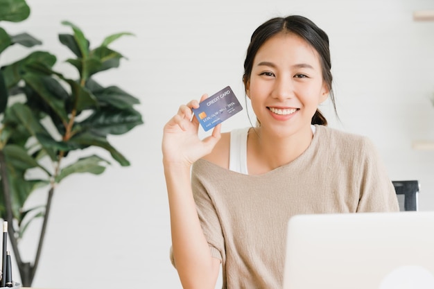 Retrato de una mujer sonriente sosteniendo una tarjeta de crédito en una computadora portátil