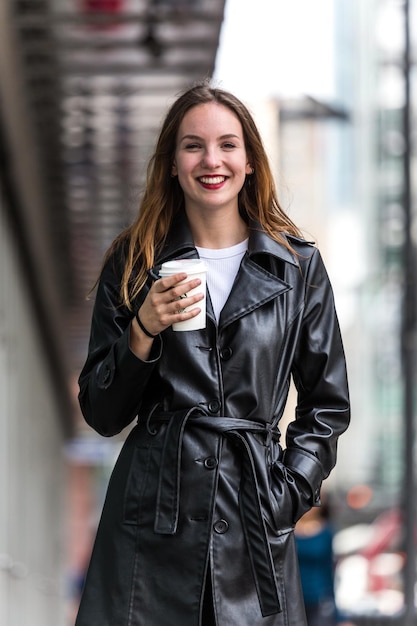 Retrato de una mujer sonriente tomando café mientras está de pie en la ciudad