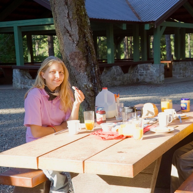 Foto retrato de una mujer sonriente tomando el desayuno en la mesa en el parque