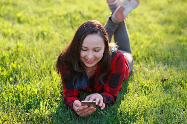 Retrato de una mujer sonriente tumbado en la hierba verde y con smartphone al aire libre