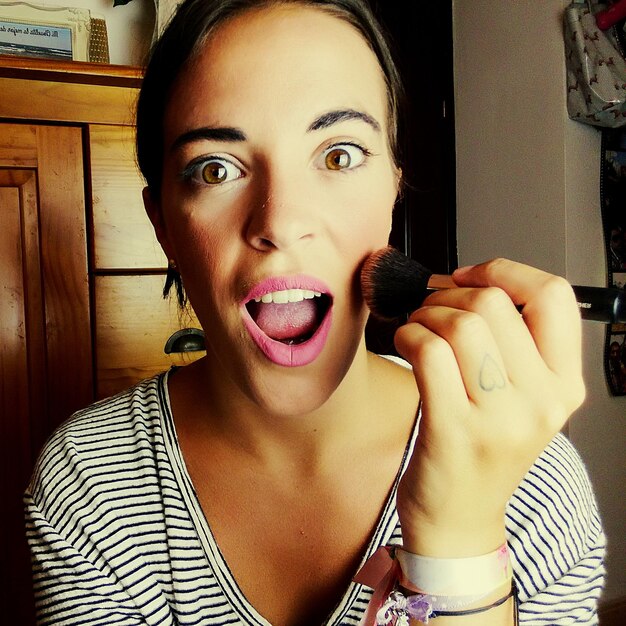 Foto retrato de una mujer sorprendida aplicando maquillaje en casa