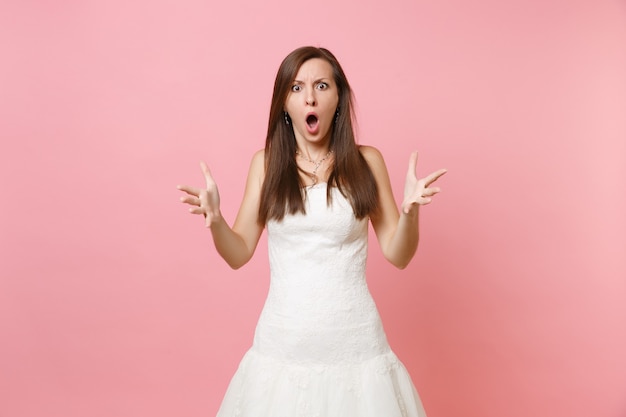 Retrato de mujer sorprendida enojada con la boca abierta en vestido blanco de pie extendiendo las manos