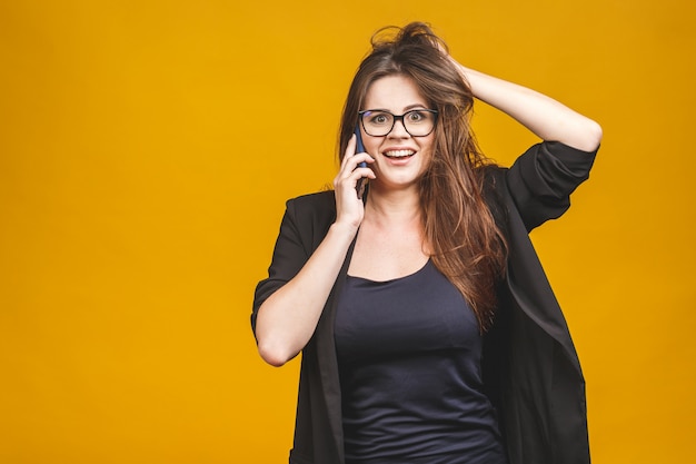 Retrato de una mujer sorprendida feliz en casual elegante hablando por teléfono sobre la pared amarilla.