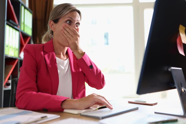 Retrato de una mujer sorprendida sentada en el lugar de trabajo y mirando la pantalla de la computadora