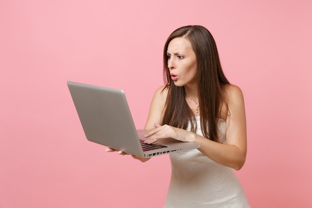 Retrato de mujer sorprendida en vestido blanco, trabajando en equipo portátil