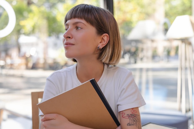 Retrato de mujer sosteniendo un cuaderno y mirando hacia otro lado