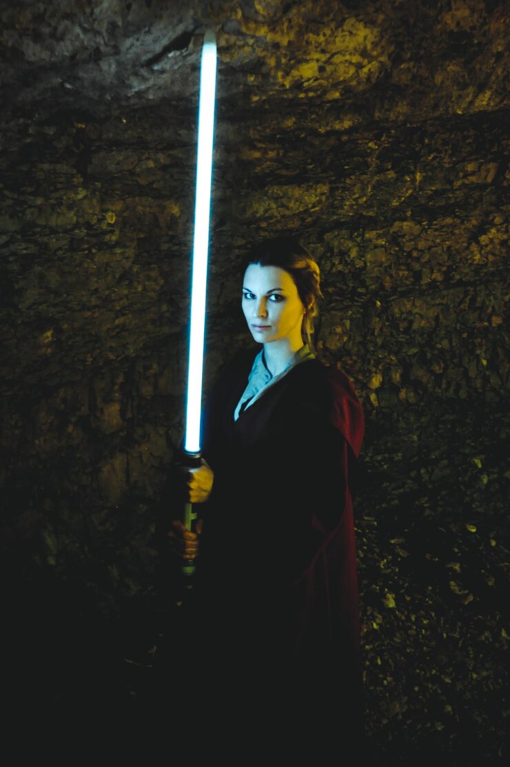 Foto retrato de una mujer sosteniendo una espada iluminada mientras está de pie junto a una roca