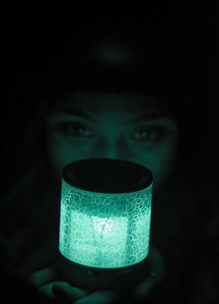 Foto retrato de una mujer sosteniendo una luz eléctrica iluminada en un cuarto oscuro