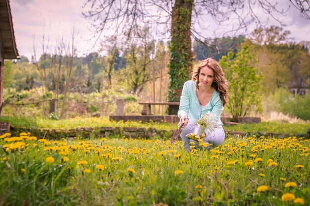 Foto retrato de una mujer sosteniendo una olla de flores mientras se agacha en medio de las plantas