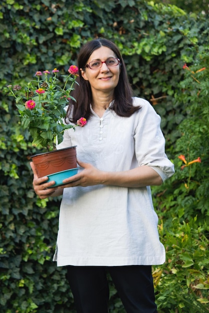 Foto retrato de una mujer sosteniendo una planta en olla mientras está de pie contra las plantas