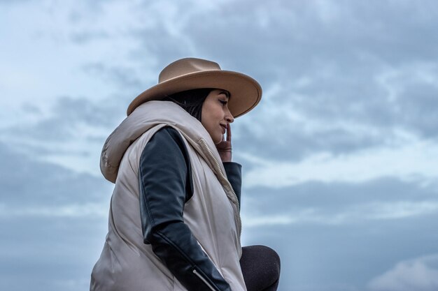 Retrato de una mujer sosteniendo su sombrero de lado con la pierna apoyada en un piso elevado al aire libre