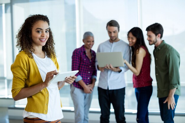 Retrato de mujer con tableta digital en la oficina mientras un colega discutiendo detrás