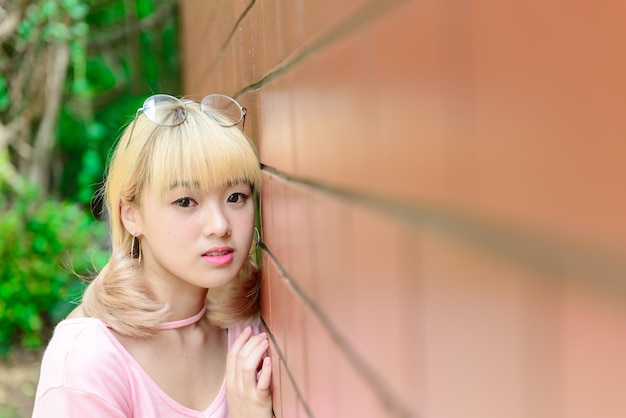 Retrato de mujer tailandesa cabellos dorados estilo japón en pared de ladrillo naranja Chica asiática posar para tomar una foto al aire libre