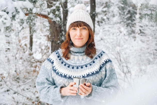 Retrato de una mujer con una taza de té en las manos sobre un fondo de bosque nevado
