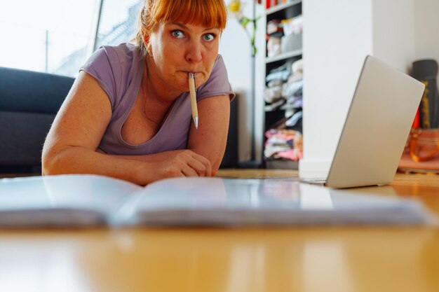 Retrato de una mujer tendida en el piso de parquet con cuadernos portátiles emociones en la cara