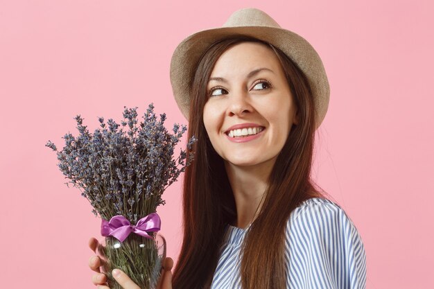 Retrato de mujer tierna joven feliz con sombrero de paja vestido azul con ramo de hermosas flores de lavanda púrpura aisladas sobre fondo rosa de tendencia brillante. Concepto de vacaciones del día internacional de la mujer