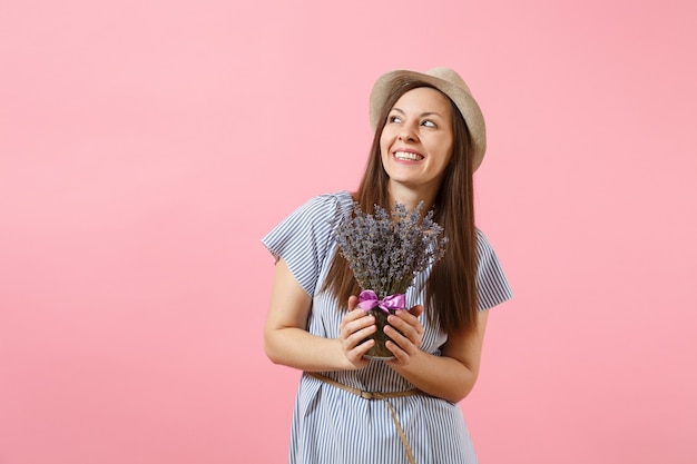 Retrato de una mujer tierna joven feliz en vestido azul, sombrero con ramo de hermosas flores de lavanda púrpura aisladas sobre fondo rosa de tendencia brillante. Concepto de vacaciones del día internacional de la mujer.