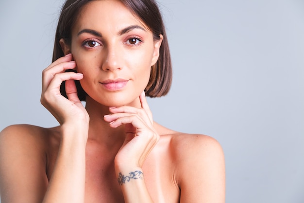 Retrato de mujer en topless con maquillaje y piel bronceada suave suave en la pared gris