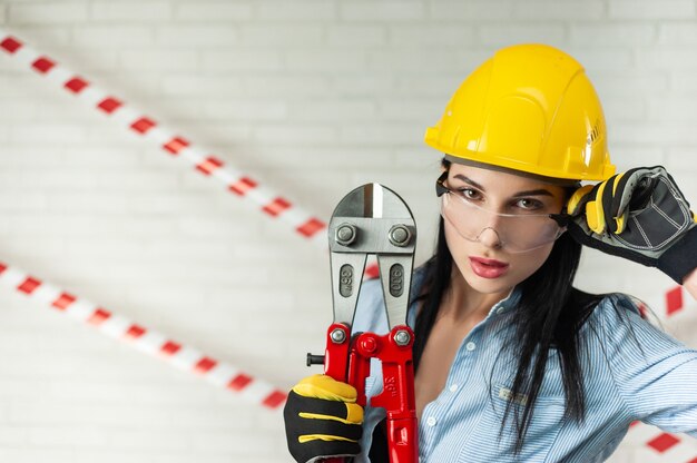 Foto retrato de una mujer trabajadora de la construcción en un casco con un cortador de pernos en sus manos