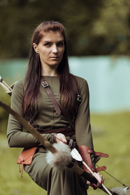 Retrato de una mujer con un traje medieval con flechas y un arco sobre un fondo borroso, primer plano